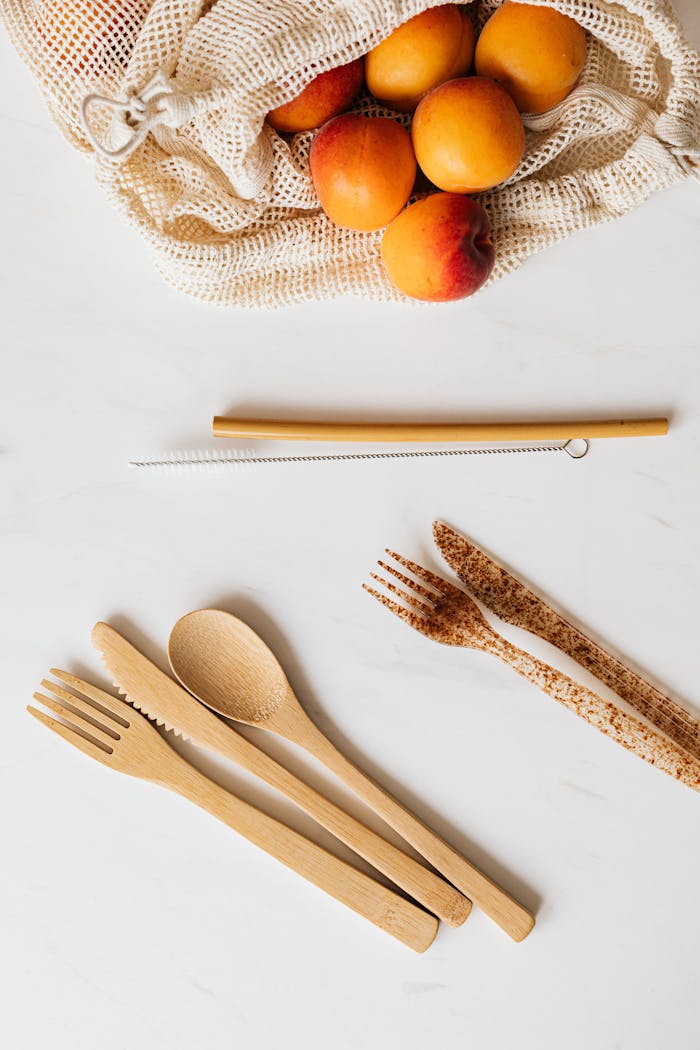 Top view of wooden and plastic cutlery placed near vivid orange peaches in cotton bag