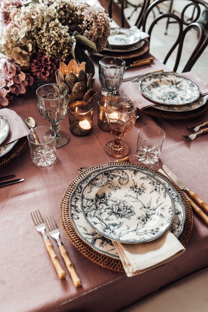 High angle of plates with cutlery placed near glassware on table decorated with burning candle and blooming flowers